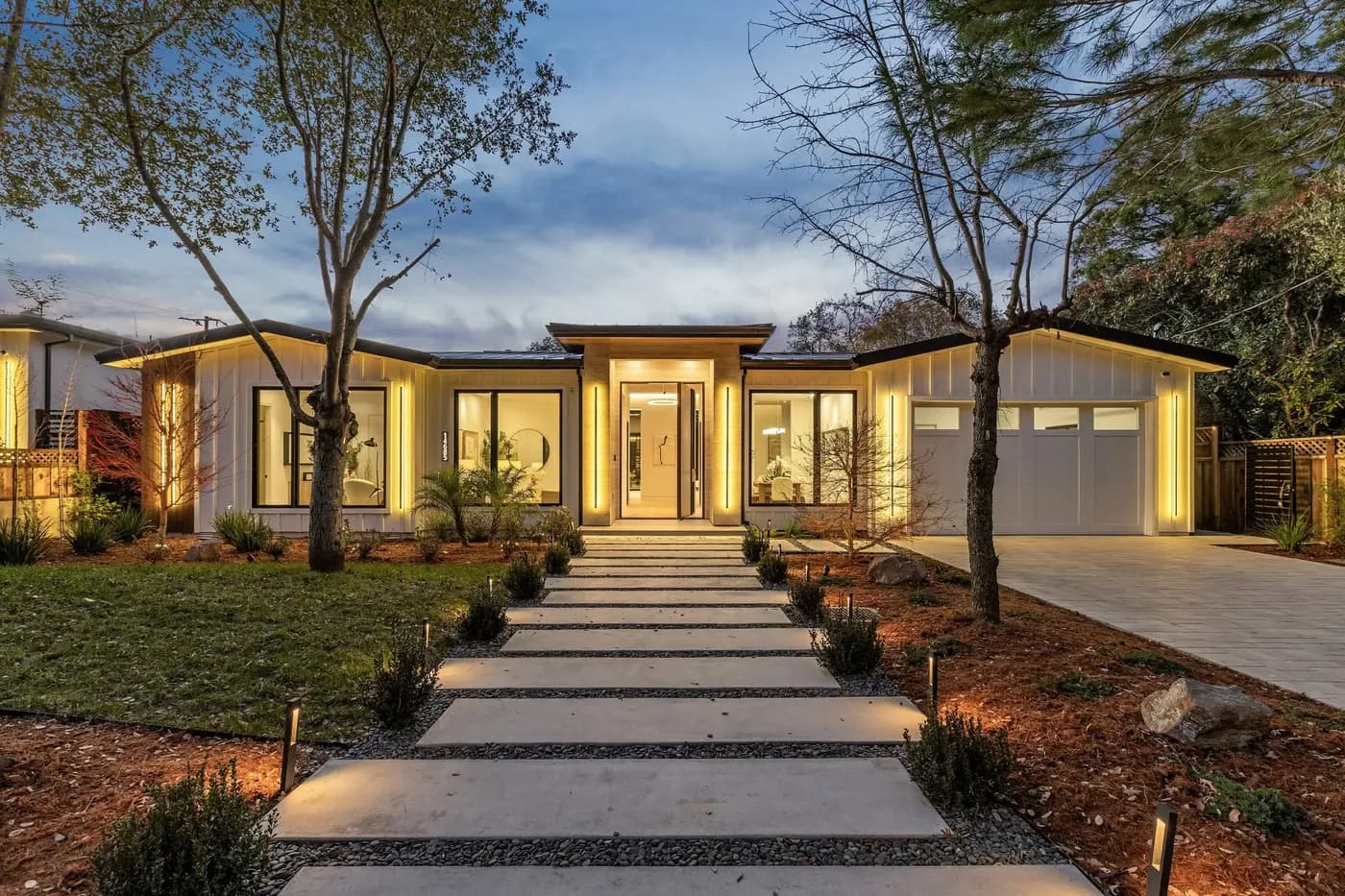 Single storey house at dusk, warm light washing the eaves and path lights to the entry