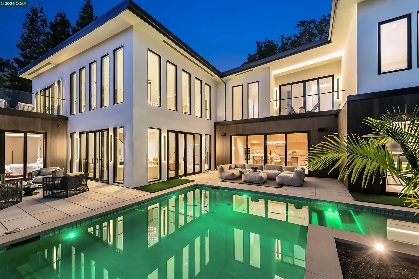 Two storey house at dusk, pool lit from within and warm light across the rear elevation