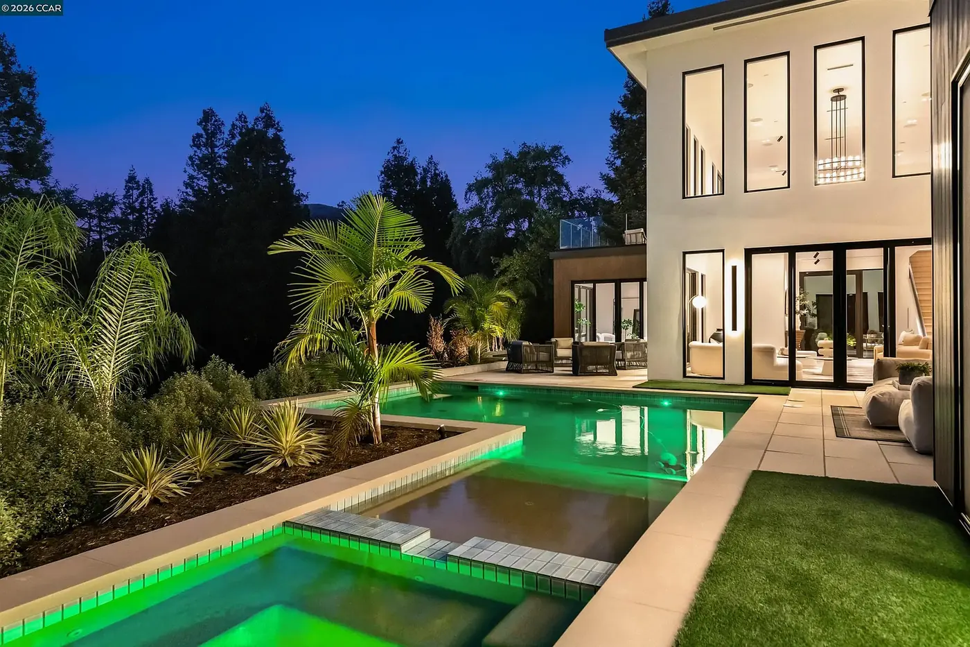 A hillside pool terrace at dusk, the water and architecture lit as one composition