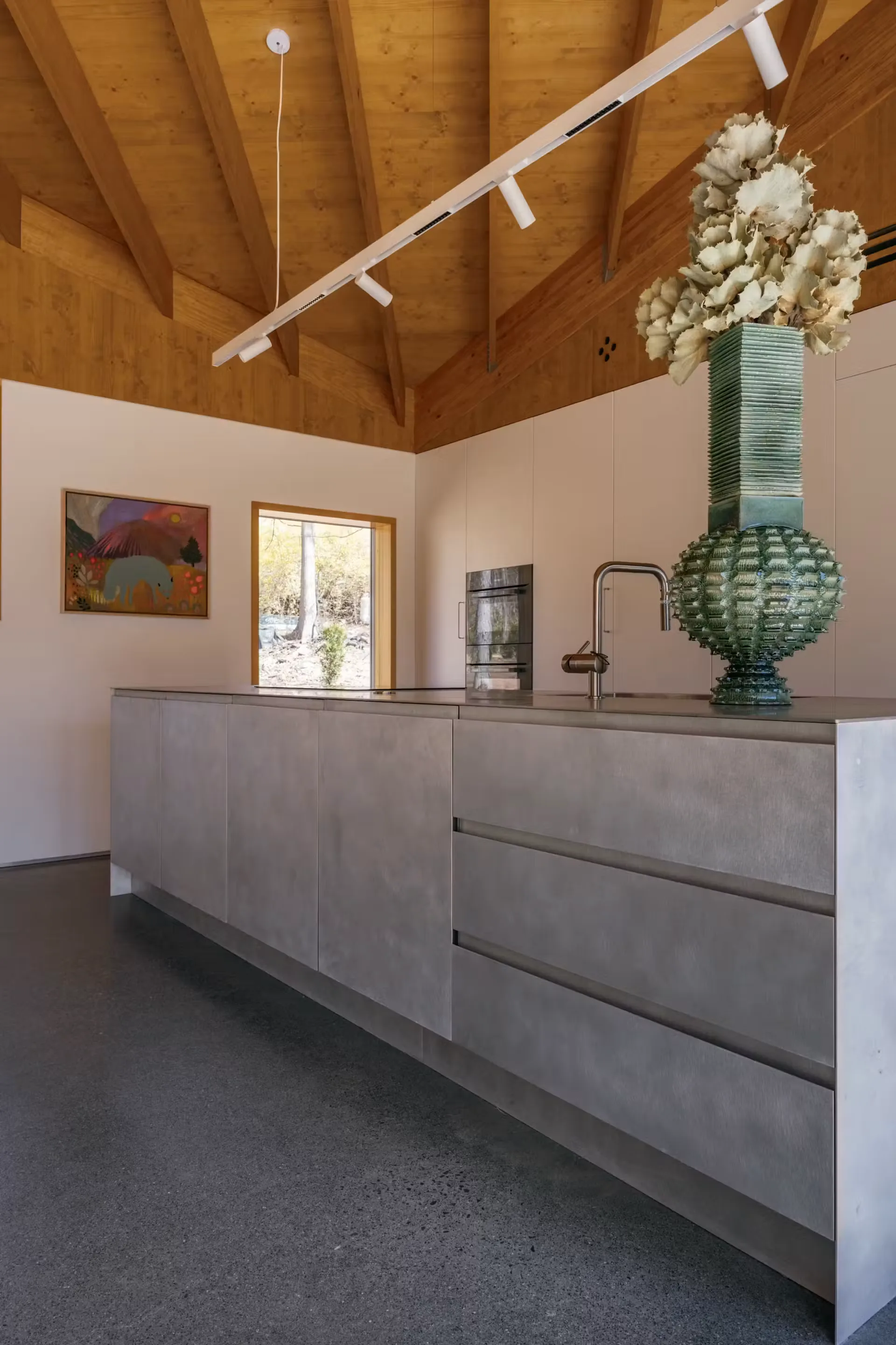 Kitchen island in pale stone with wall ovens behind