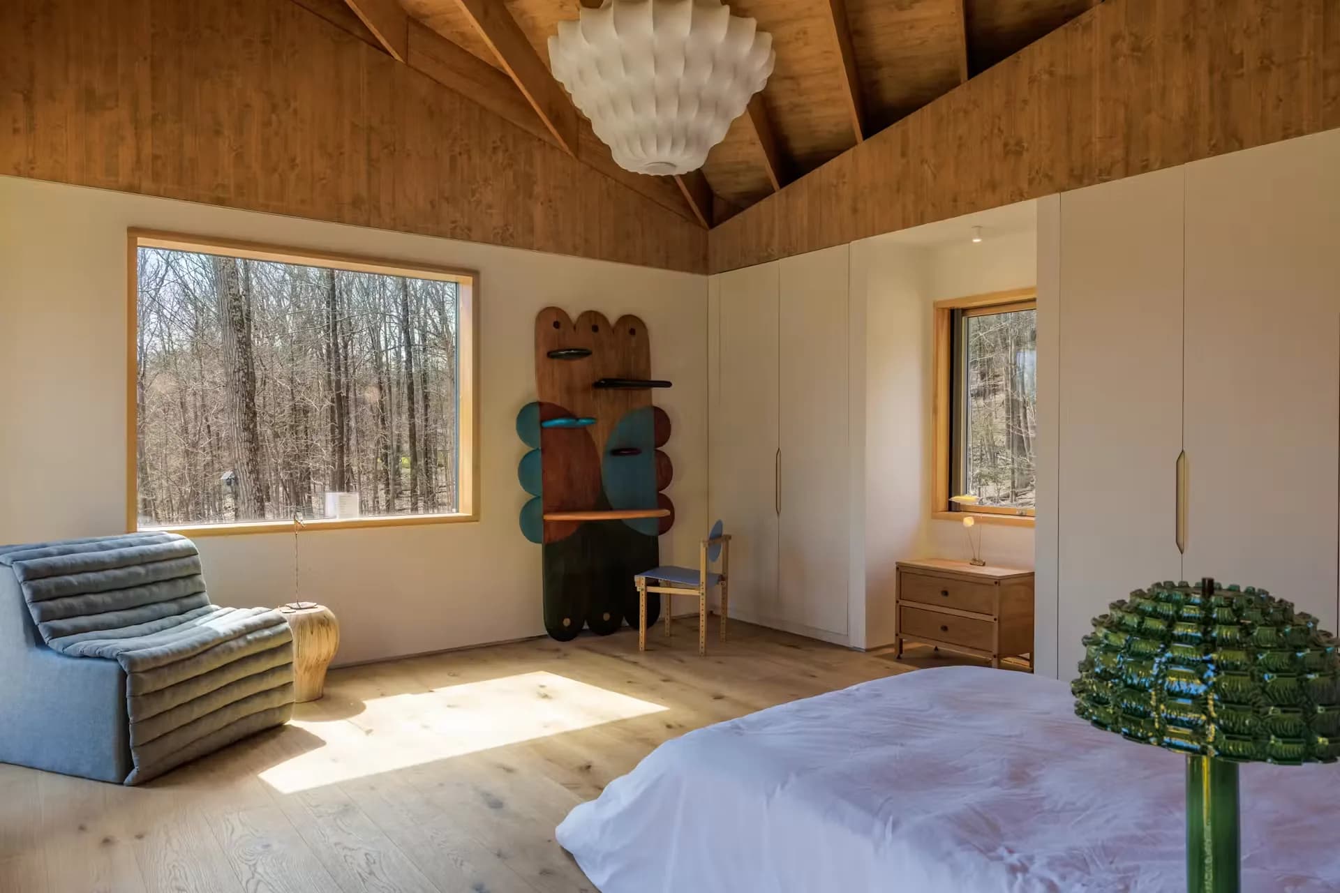 Bedroom under the timber ceiling with a wide window onto the trees
