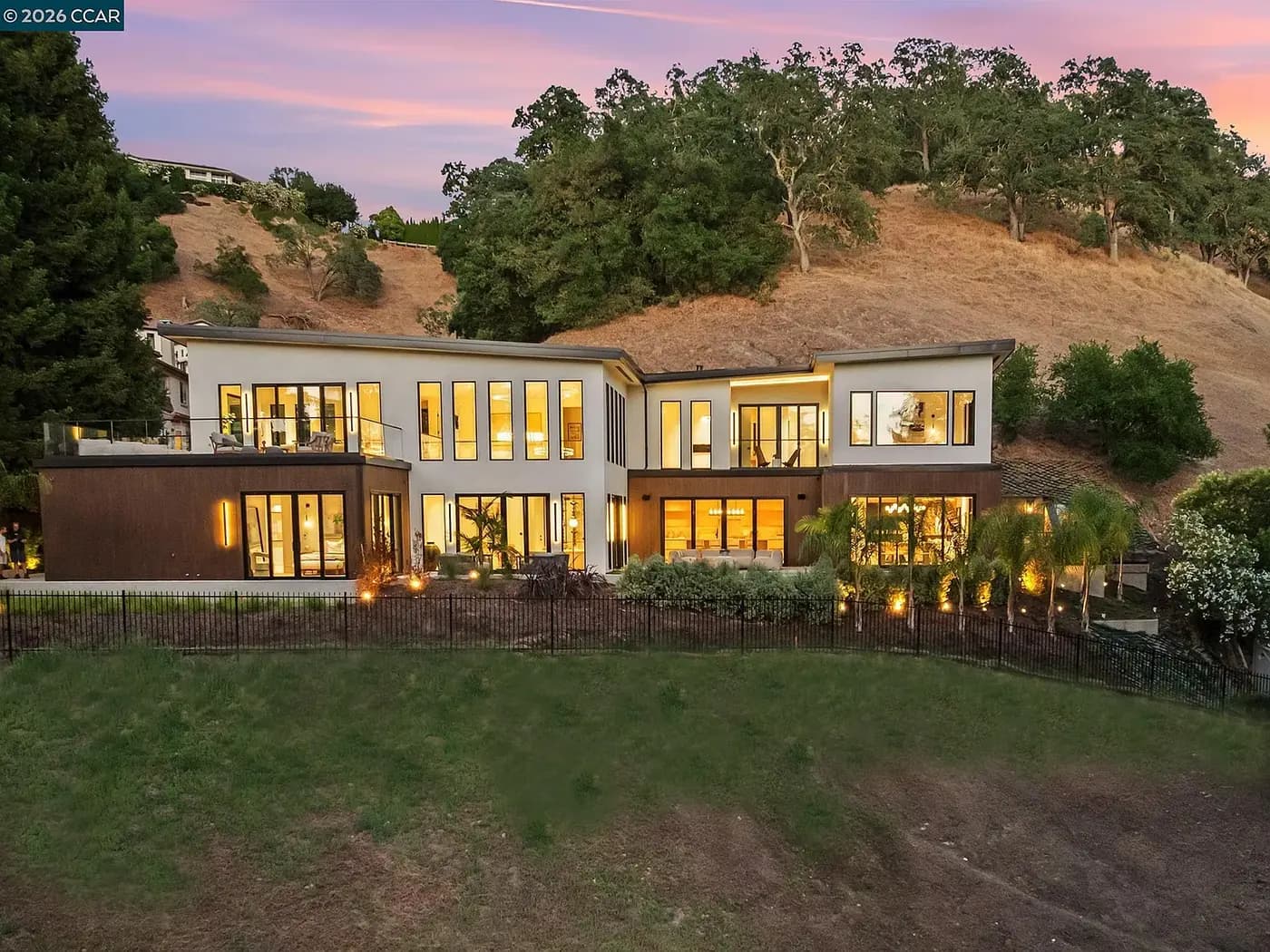 Rear elevation at dusk, windows lit against the hillside